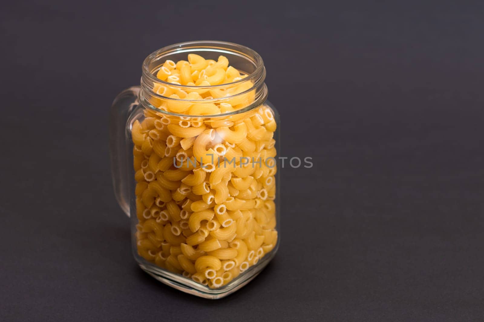 Uncooked Chifferi Rigati Pasta in Glass Jar on Black Background. Fat and Unhealthy Food. Classic Dry Macaroni. Italian Culture and Cuisine. Raw Pasta