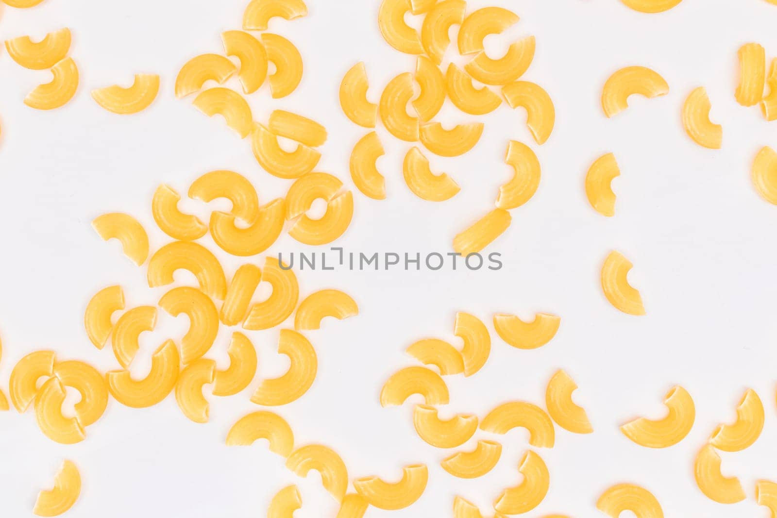 Scattered Uncooked Chifferi Rigati Pasta on White Background. Fat and Unhealthy Food. Classic Dry Macaroni Texture. Italian Culture and Cuisine. Raw Pasta