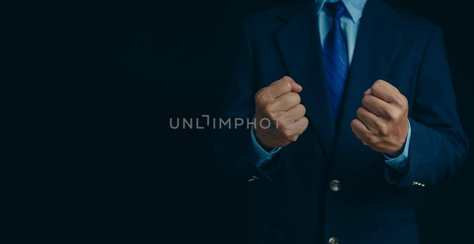Businessman in a suit stands and makes a fist gesture on a dark background.