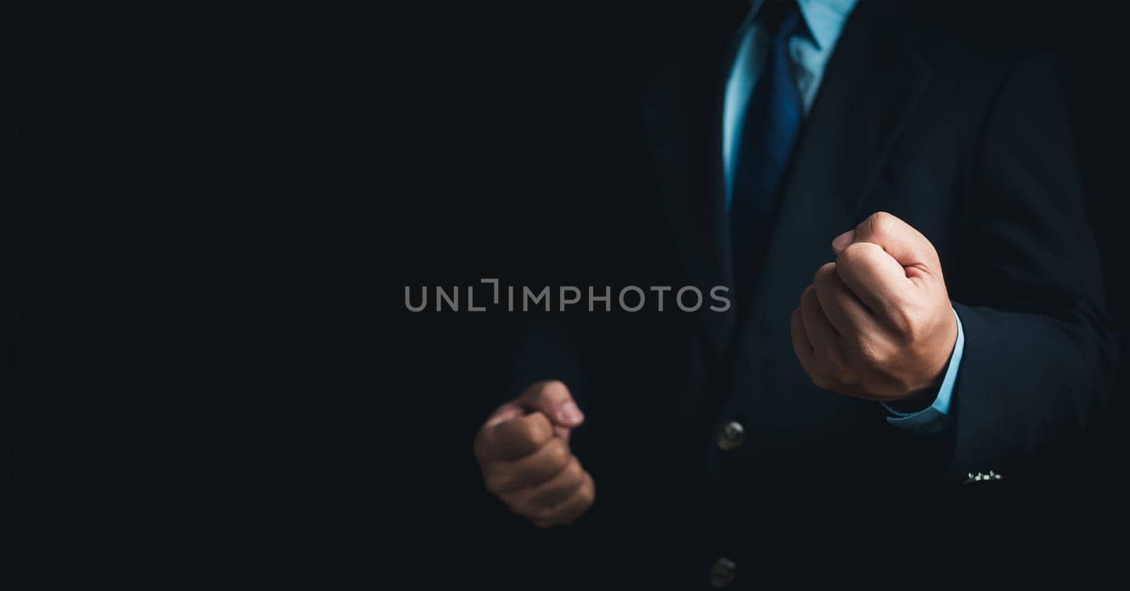 Businessman in a suit stands and makes a fist gesture on a dark background.