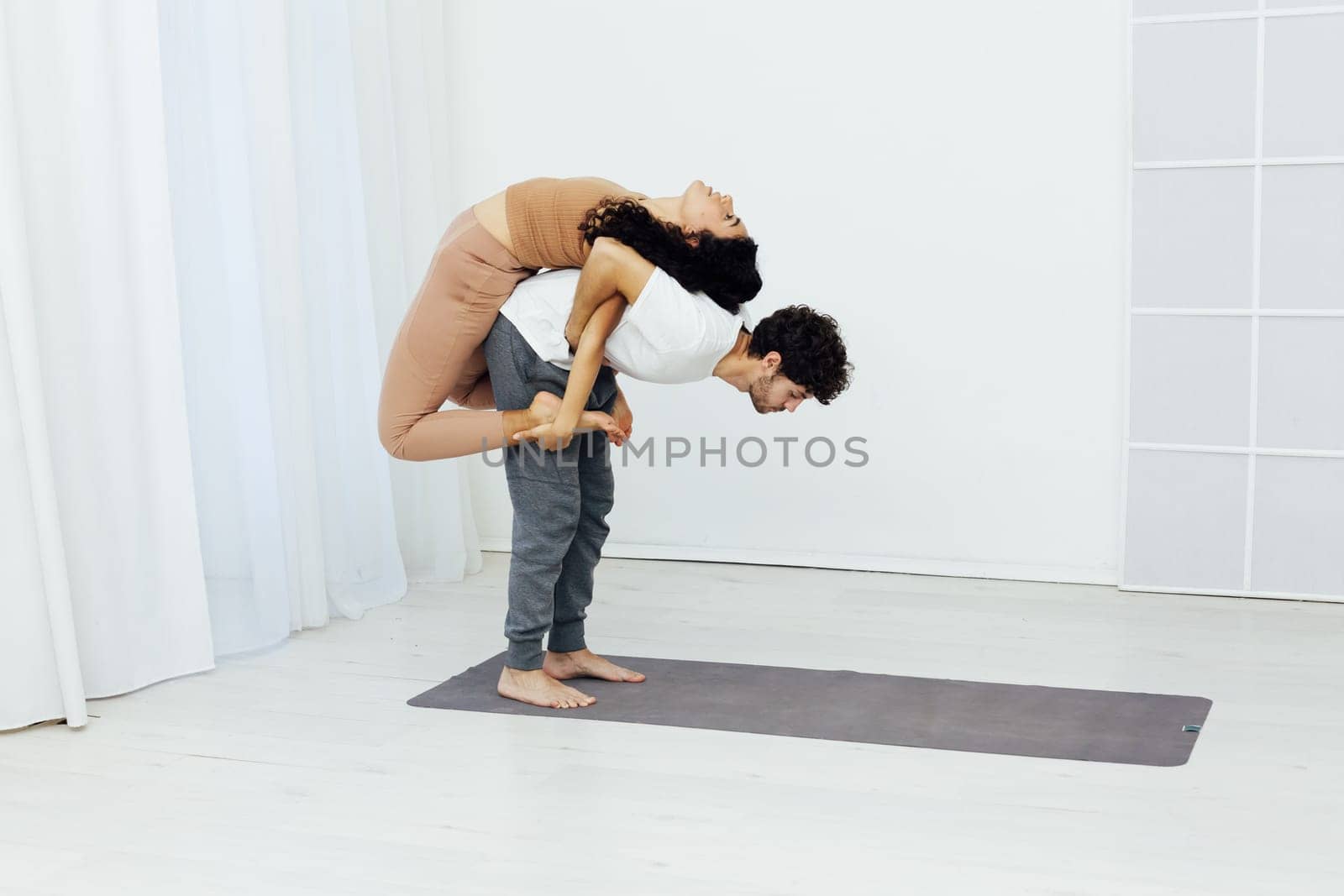 Yoga group concept. Young couple meditating together, sitting back to back on windows background