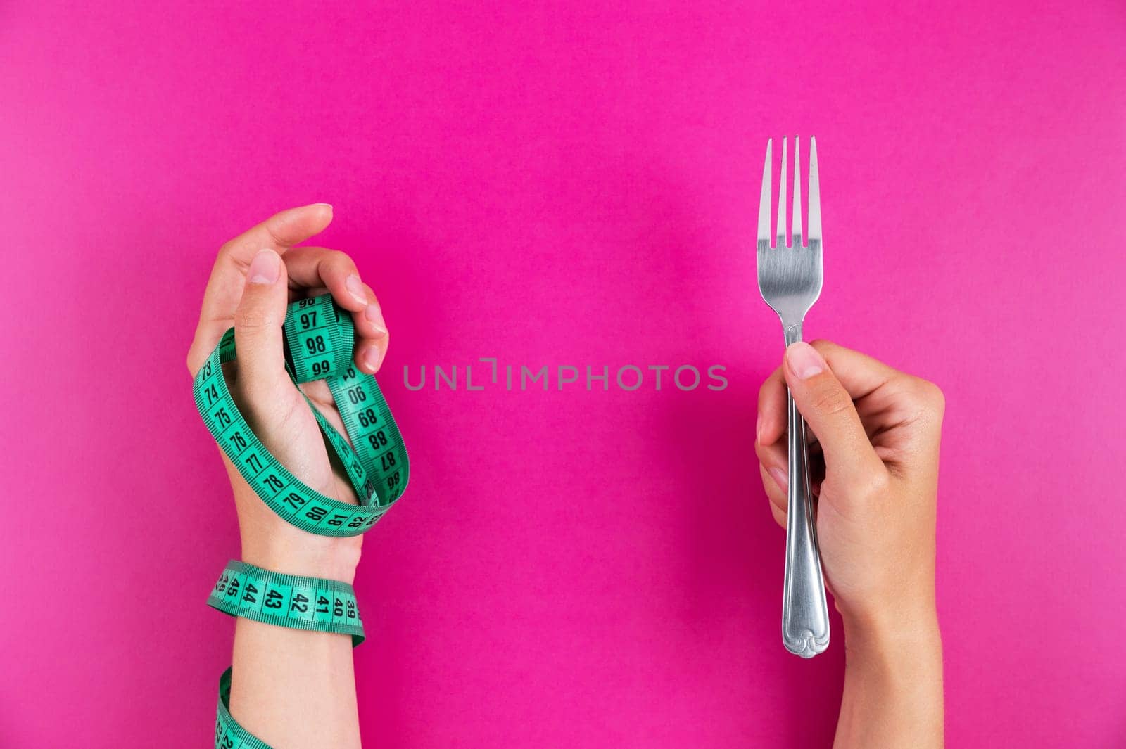 Close-up of a hand with a measuring tape wrapped around it and a fork in the other hand. Diet and healthy eating concept by yanik88