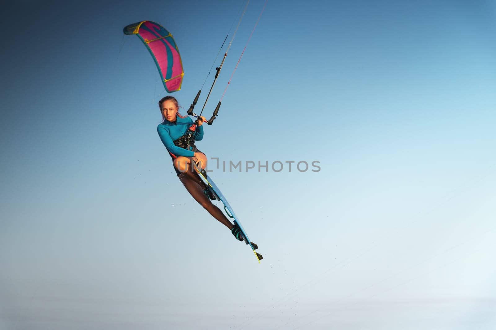 Caucasian woman kitesurfer athlete doing a trick in the air against a blue sky without a cloud. Professional kitesurfing training.