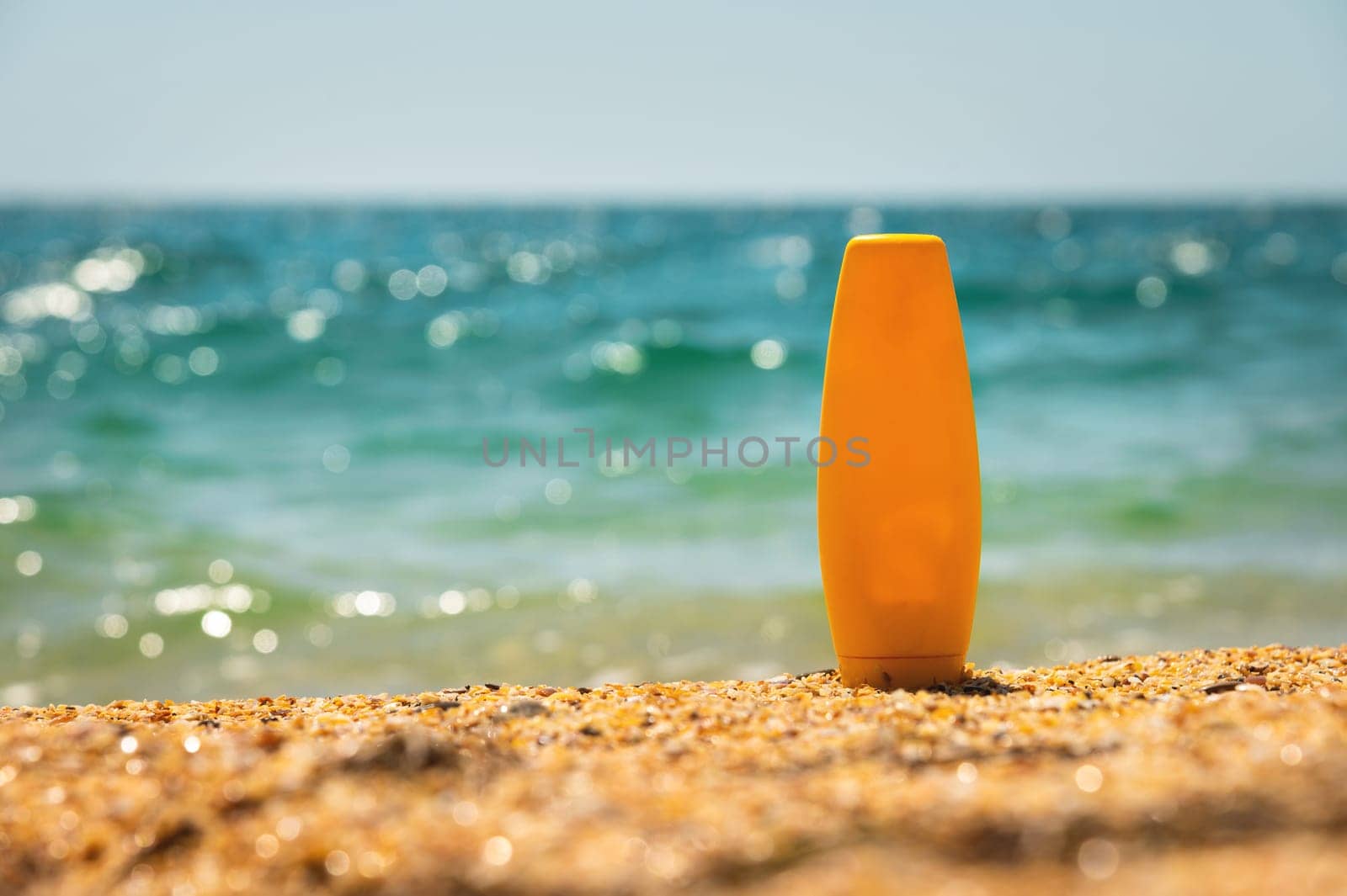 empty cosmetic skin care cream or sunscreen on sandy beach on sea background. a yellow bottle of cream stands on the sand. Blank template for brand presentation by yanik88