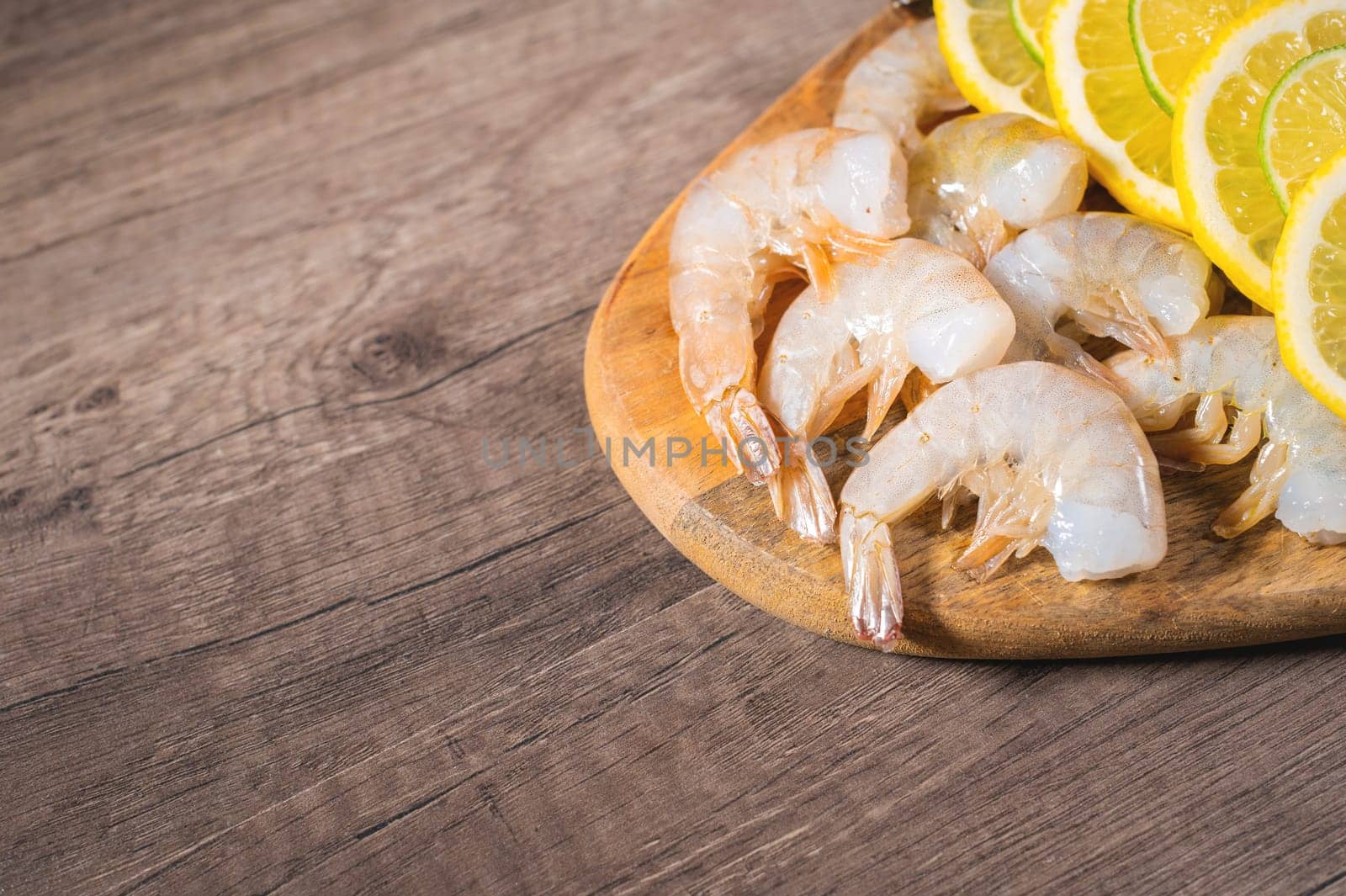 boiled shrimp on a wooden plate or cutting board. cooked food with lemon spices on a wooden table in a seafood restaurant by yanik88