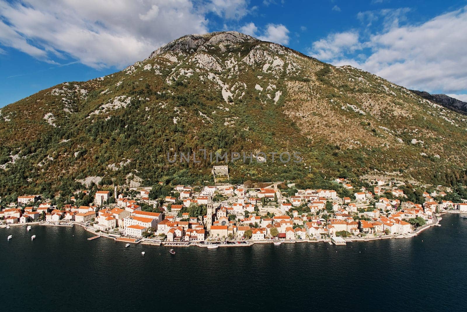 Winding coastline of Perast with the bell tower of the church at the foot of the mountain. Montenegro. Drone. High quality photo