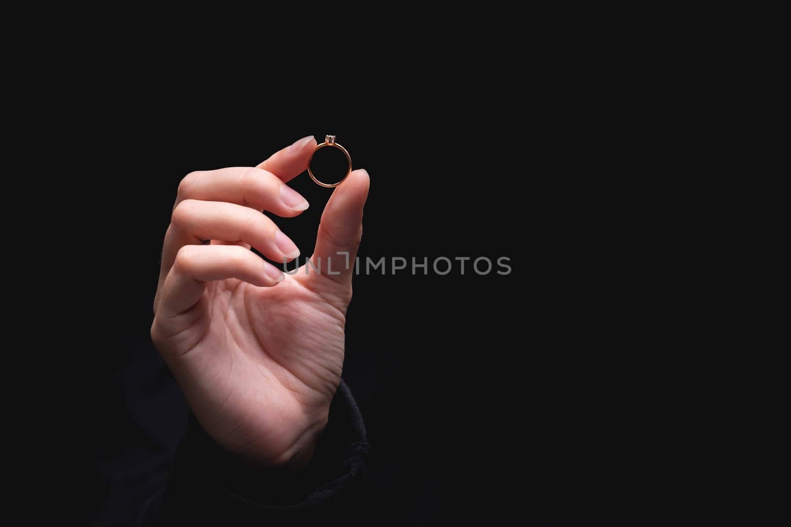 Diamond ring in the hand of a young woman on a black background. Concept of love and wedding or divorce and unsuccessful marriage.