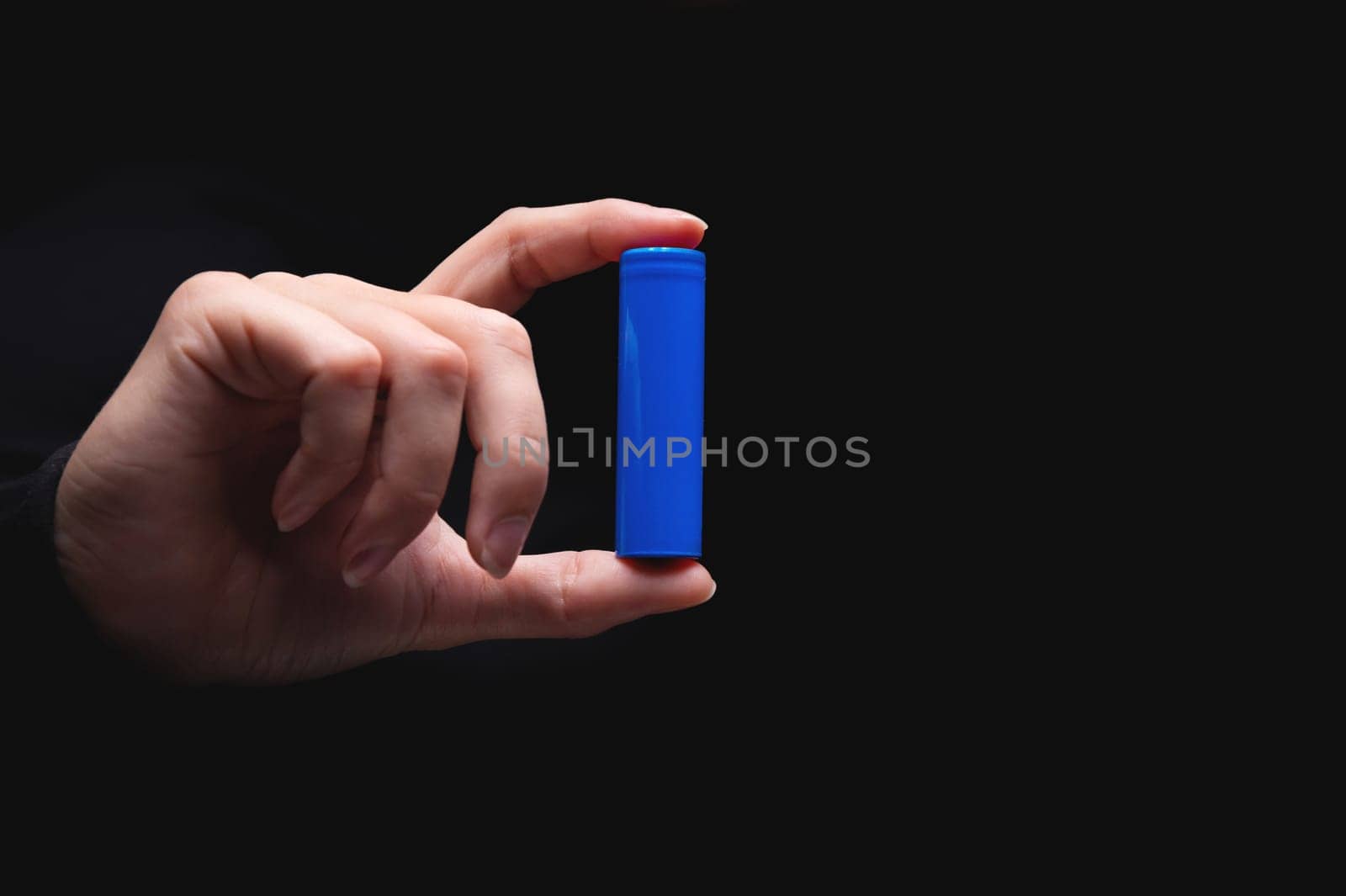 Close-up of a man's hand holding a battery on a black background. Preparing to recycle your lithium battery. Lithium battery mockup by yanik88