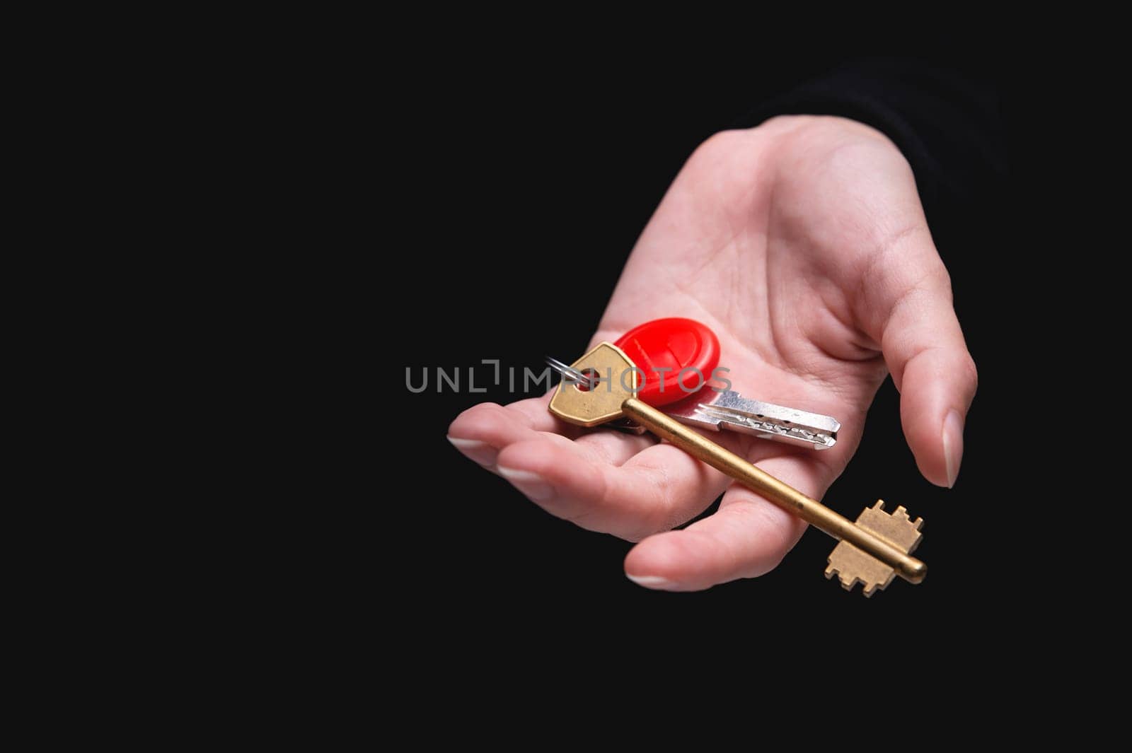 hand on a black background gives a key to a new house, holds a keychain and offers an apartment for rent. Homeowner and tenant, buying your own home, renting a property by yanik88