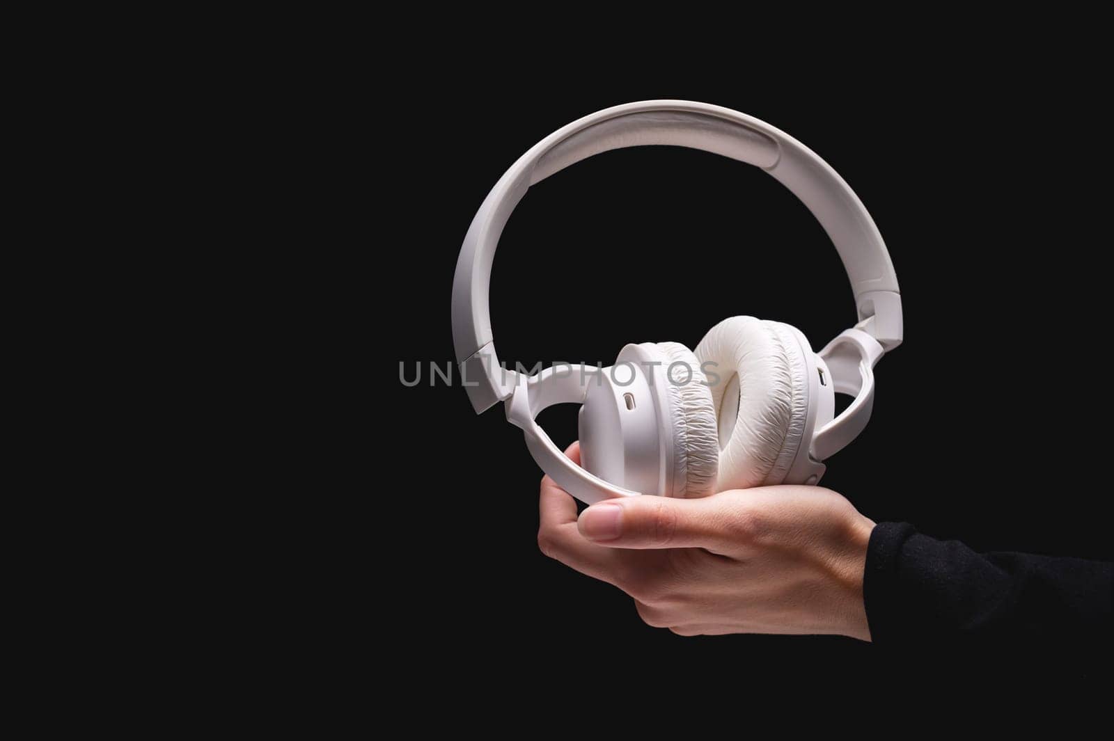 Wireless headphones on a black background. White full-size noise-canceling headset with built-in microphone. Side view of acoustic stereo sound system in female hand by yanik88