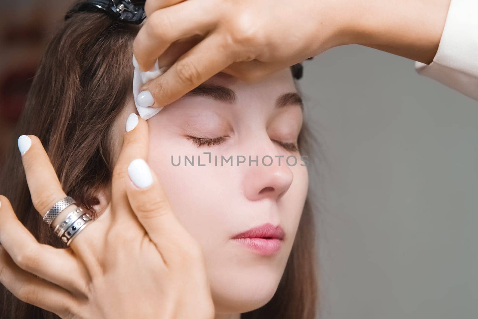 girl washes paint off her eyebrow. A female cosmetologist wipes makeup off a client's face with a cotton pad. Cosmetologist, makeup concept, beauty salon plan by yanik88