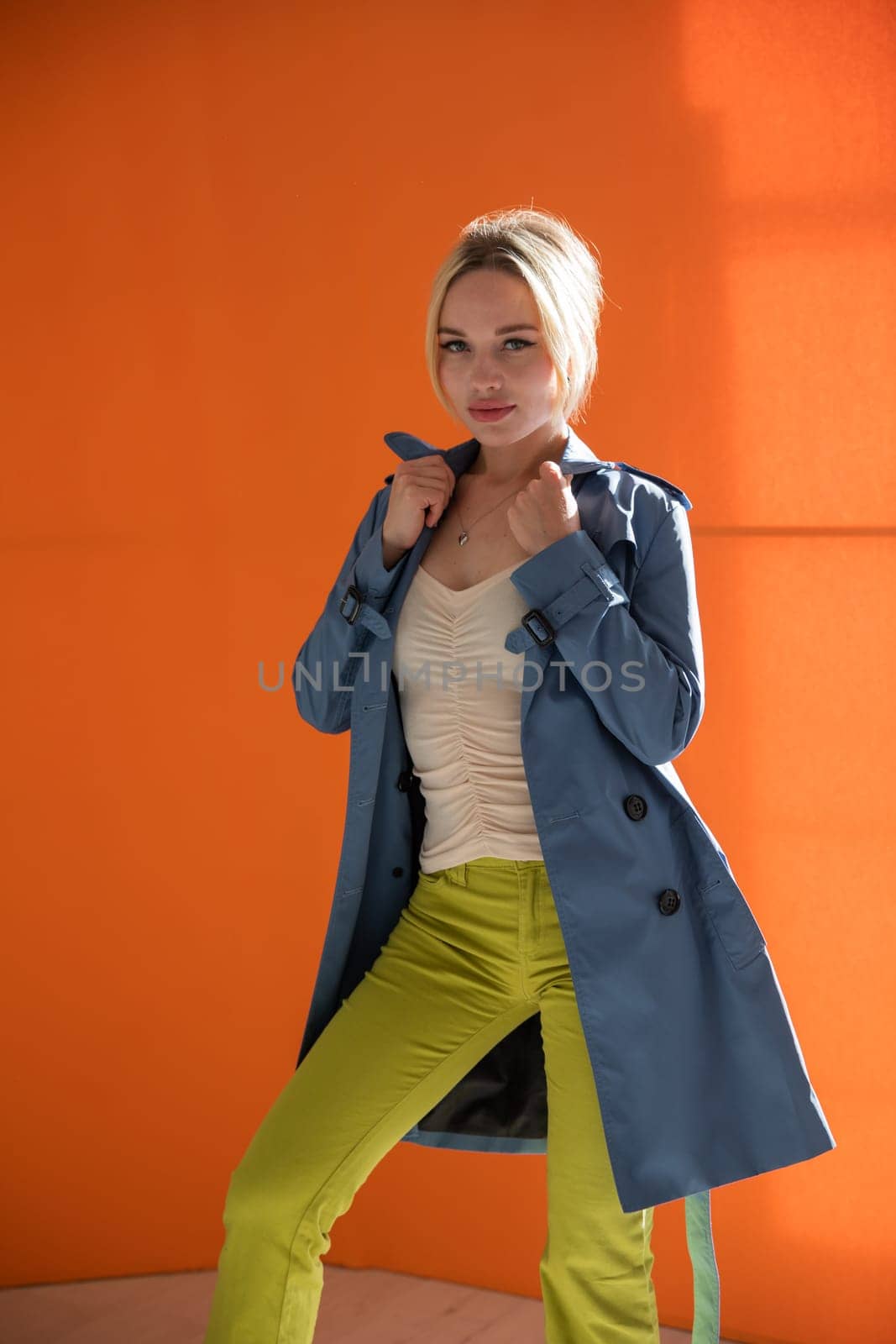 Blonde woman in autumn raincoat on orange background