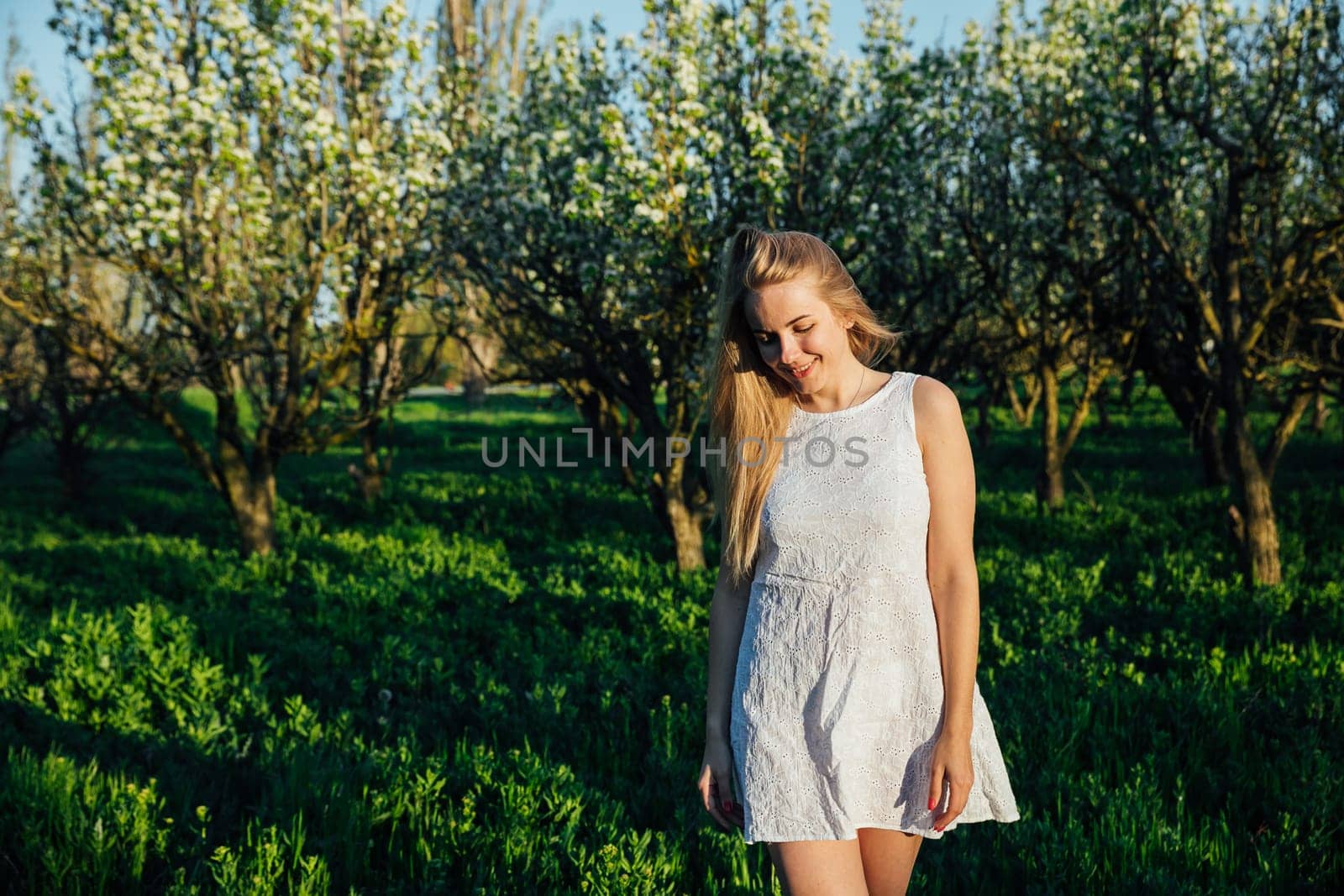 Beautiful blonde woman walking in blooming garden in spring by Simakov