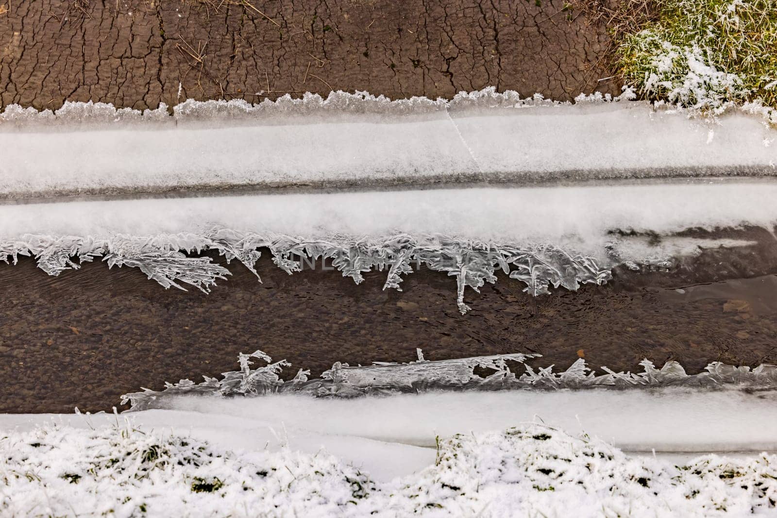 A stream bank with filigree crystals and formations of frozen water and ice