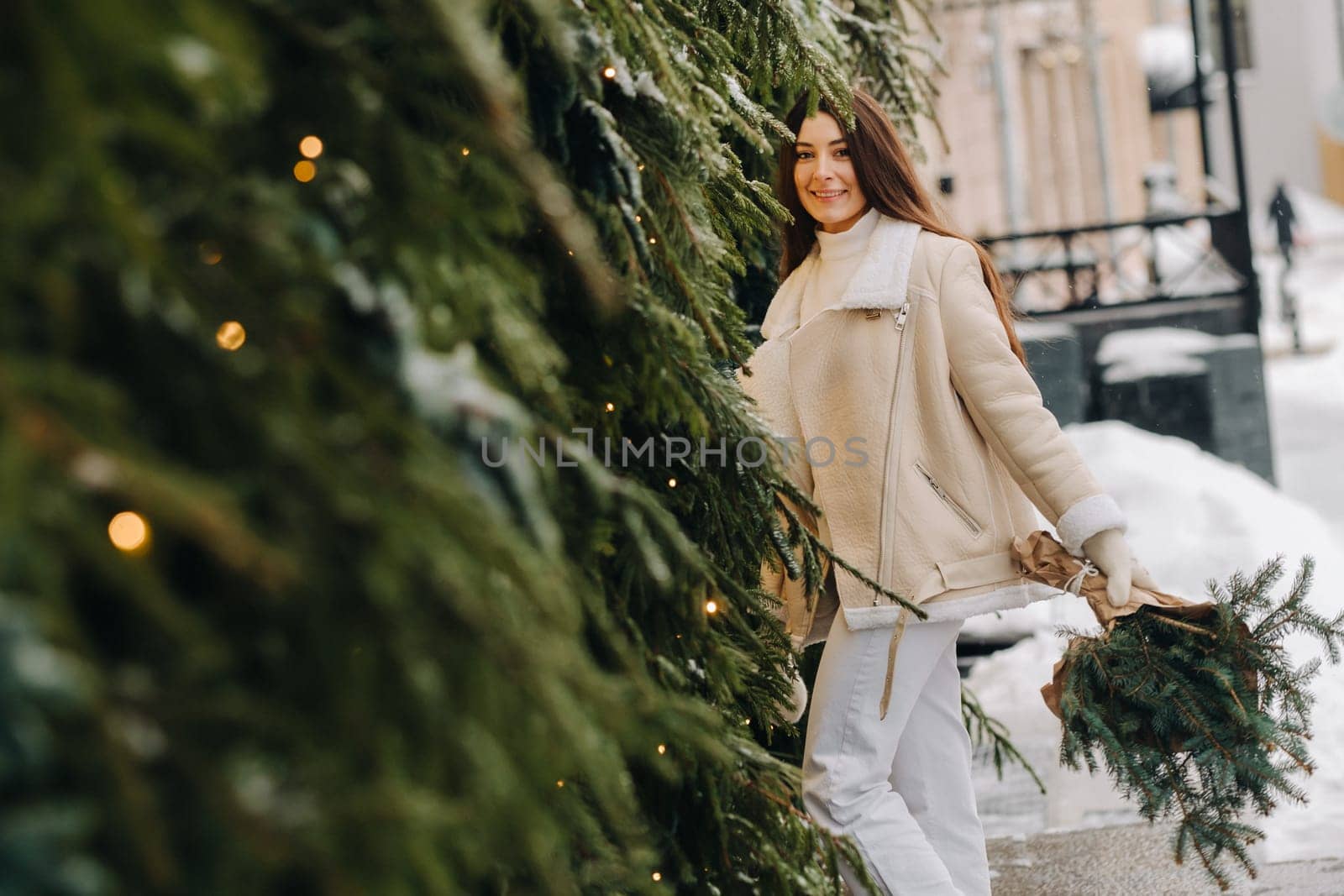 A girl with long hair in winter on the street with a bouquet of fresh fir branches.