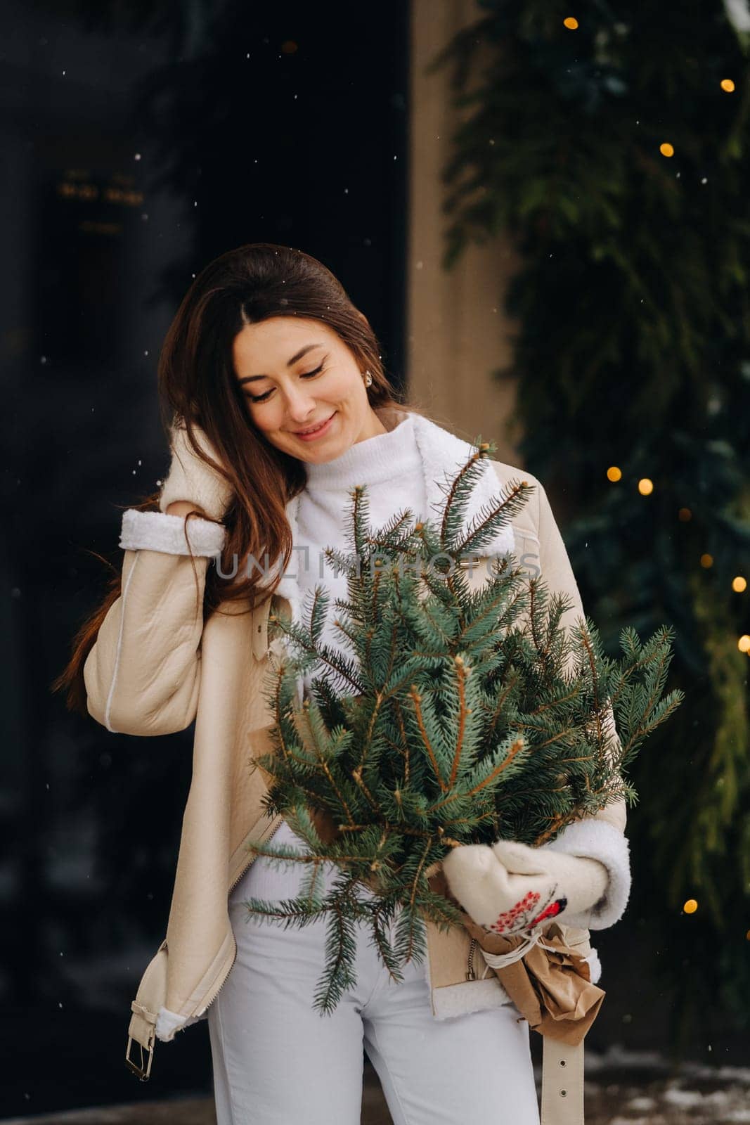 A girl with long hair in winter on the street with a bouquet of fresh fir branches.