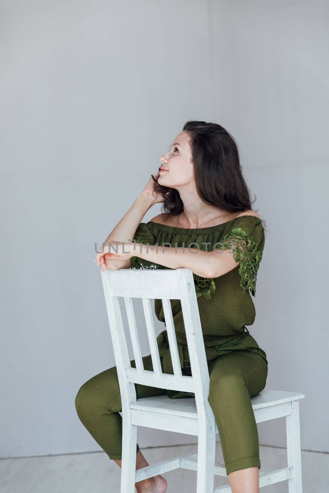 Portrait of a beautiful brunette woman in green clothes on a white chair by Simakov