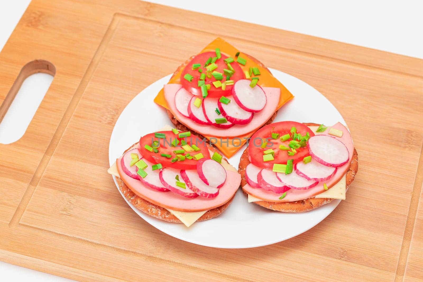 Crispy Cracker Sandwiches with Tomato, Sausage, Cheese, Green Onions and Radish on White Plate. Easy Breakfast. Quick and Healthy Sandwiches. Crispbread with Tasty Filling. Healthy Dietary Snack