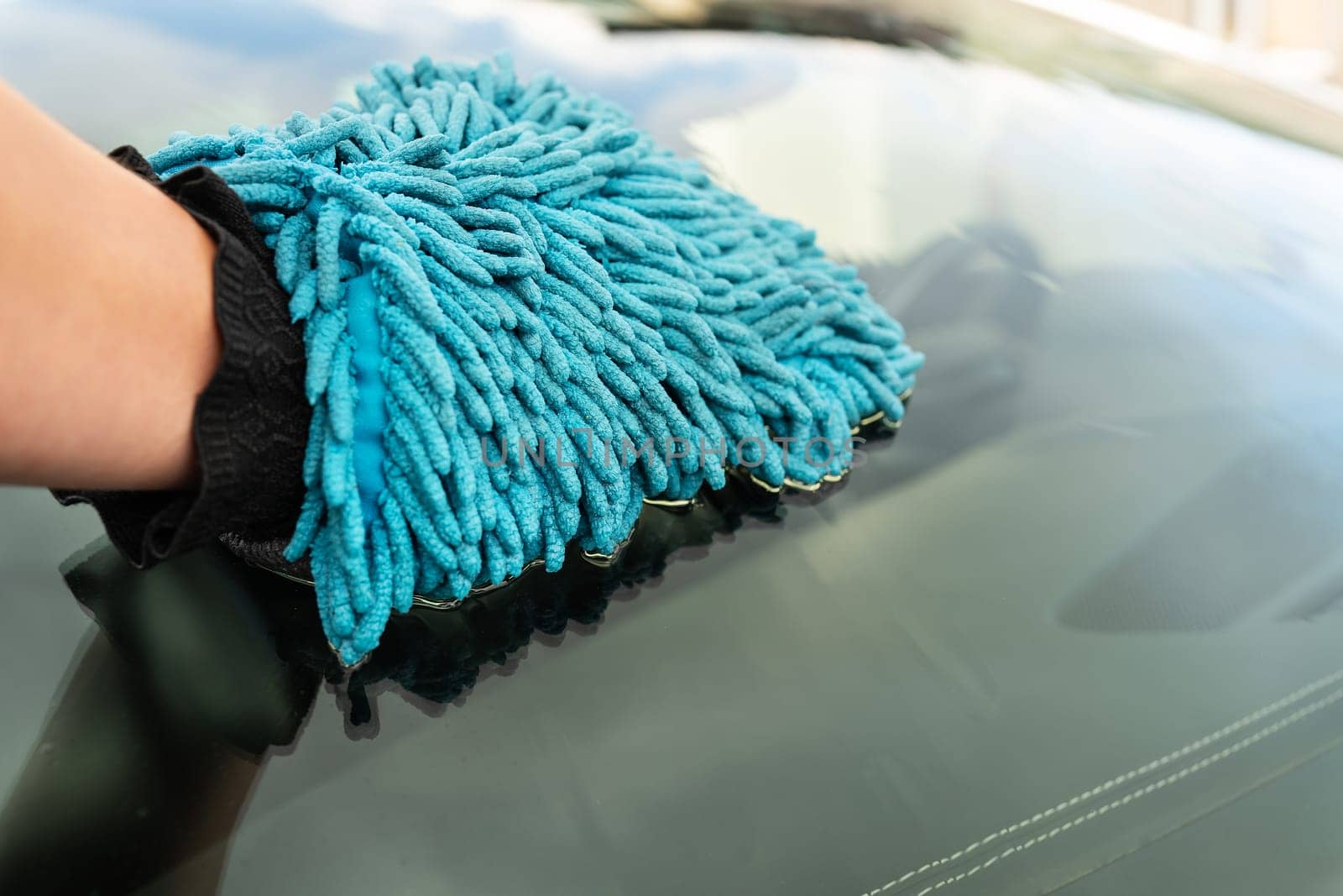 Car wash and self-service concept. A man washes the car windshield with a large blue washcloth