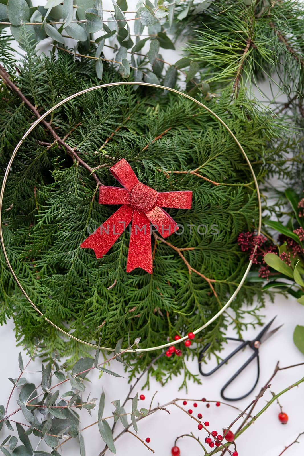 Christmas wreath with red bow and berries on a white background with greenery and scissors