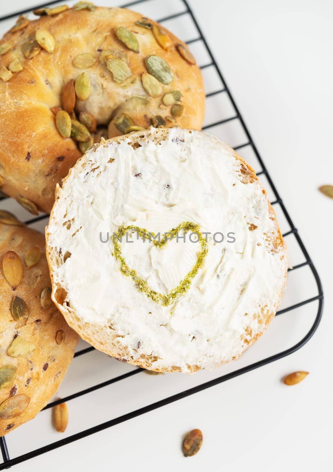 Round bread with cream cheese and a heart made of pesto on a white background