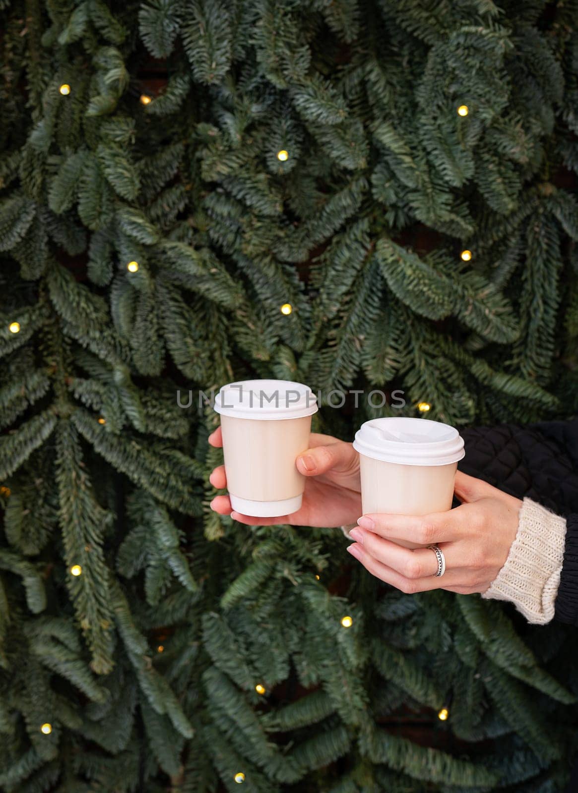 Two hands holding paper cups of coffee in front of a Christmas tree