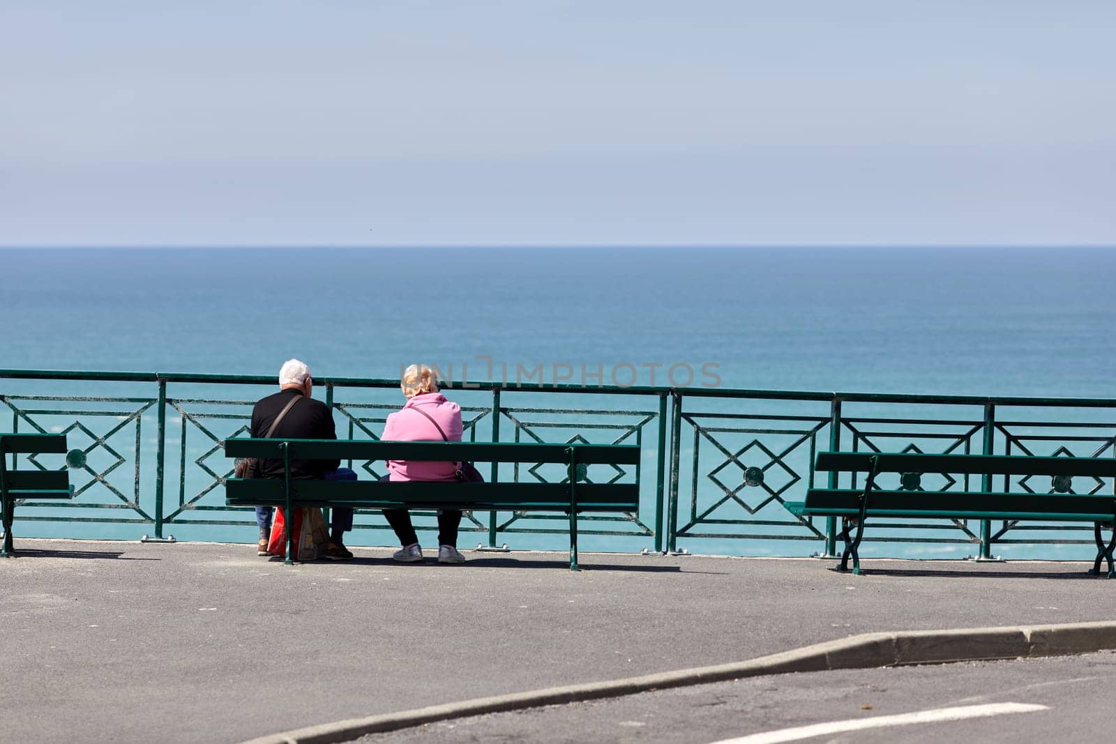 couple sitting on a bench looking at the sea by lhorintson