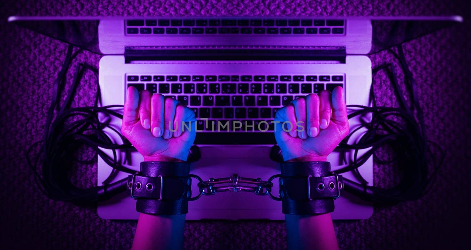 the female sexy hands in bdsm handcuffs with laptop in neon light on dark background