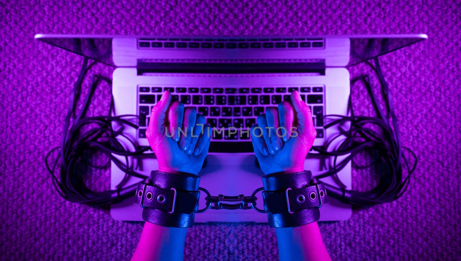 female sexy hands in bdsm handcuffs with laptop in neon light on dark background by Rotozey