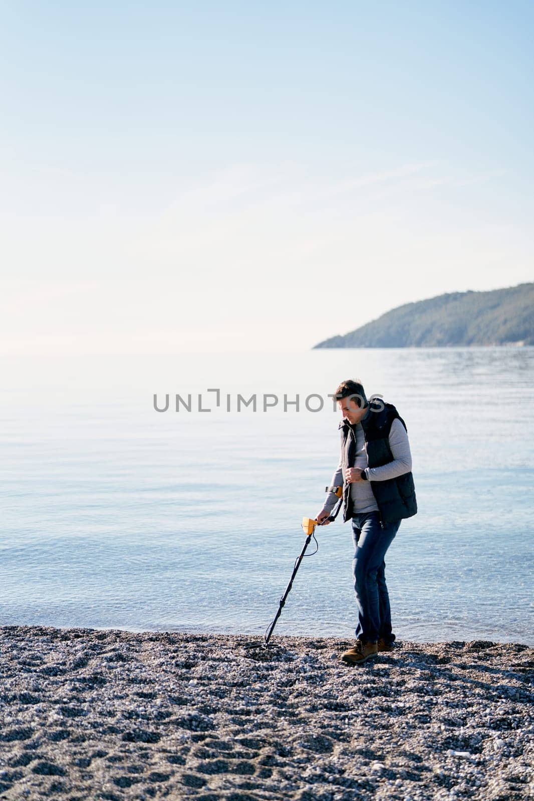 Beach cop with a metal detector and headphones walks along the beach by the sea. High quality photo