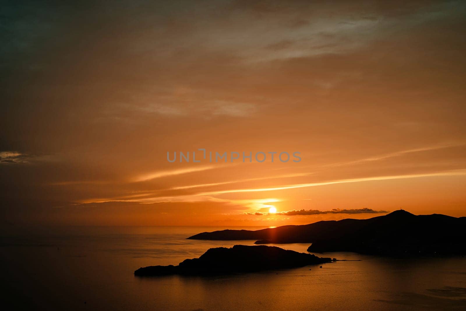 Orange sunset over silhouettes of mountains by the sea. High quality photo