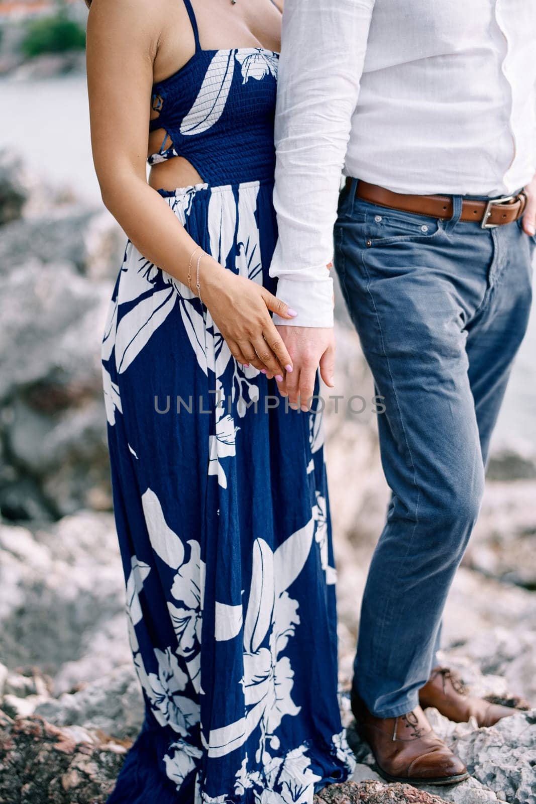 Man and woman stand with their hands touching on the stones. Cropped. Faceless. High quality photo