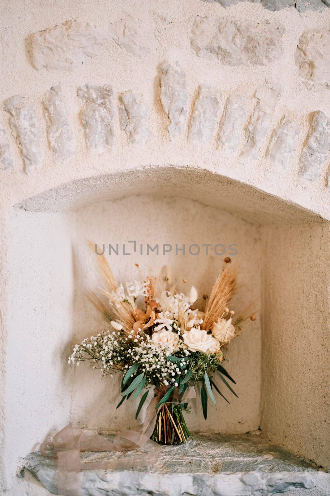 Bride bouquet stands in a niche of an ancient stone house by Nadtochiy