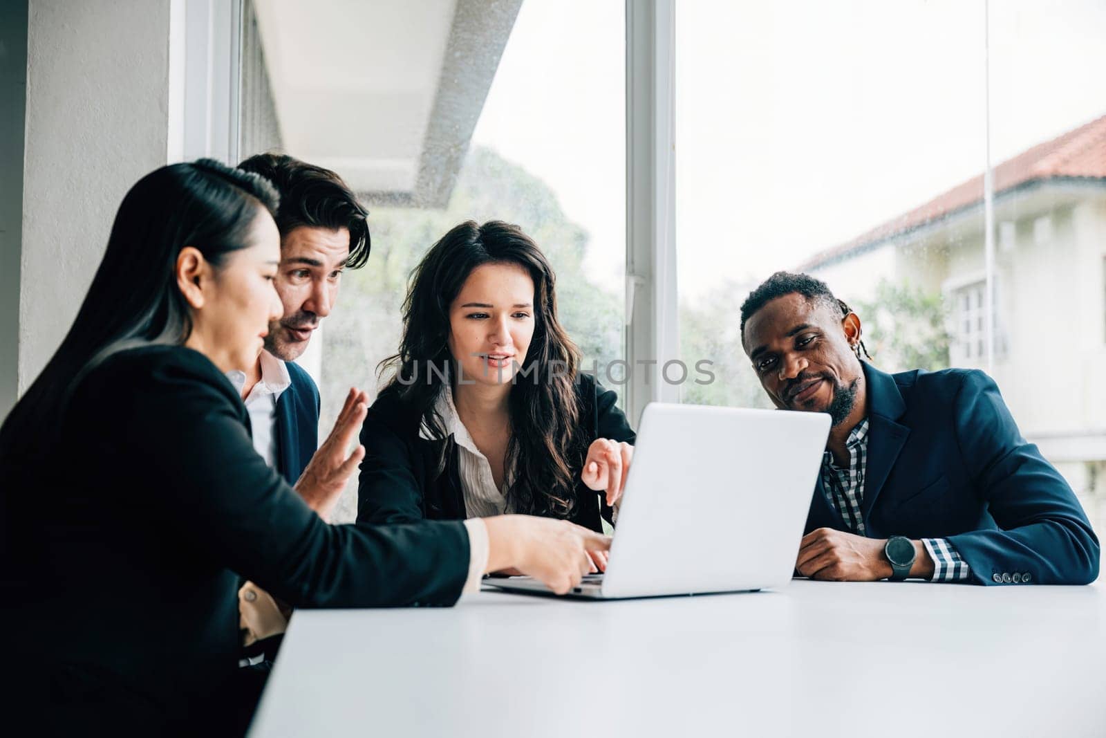 In an office meeting room, both men and women from diverse business team work together on laptop. Their teamwork, diversity and collaboration are palpable they discuss plan and strategize for success. by Sorapop