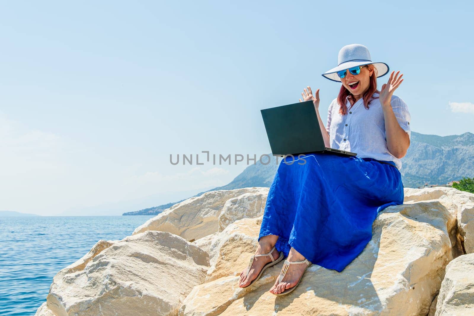 Young woman enjoys a remote working day at the beach, typing on her laptop with the ocean in the background, combining work and leisure.