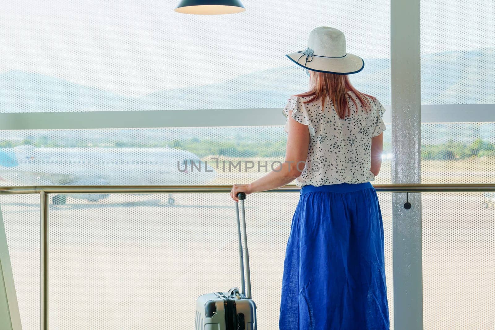 A young girl standing by a wide airport window, looking out at the runway and reflecting on her upcoming vacation. The natural light creates a serene atmosphere as the girl gazes outside.