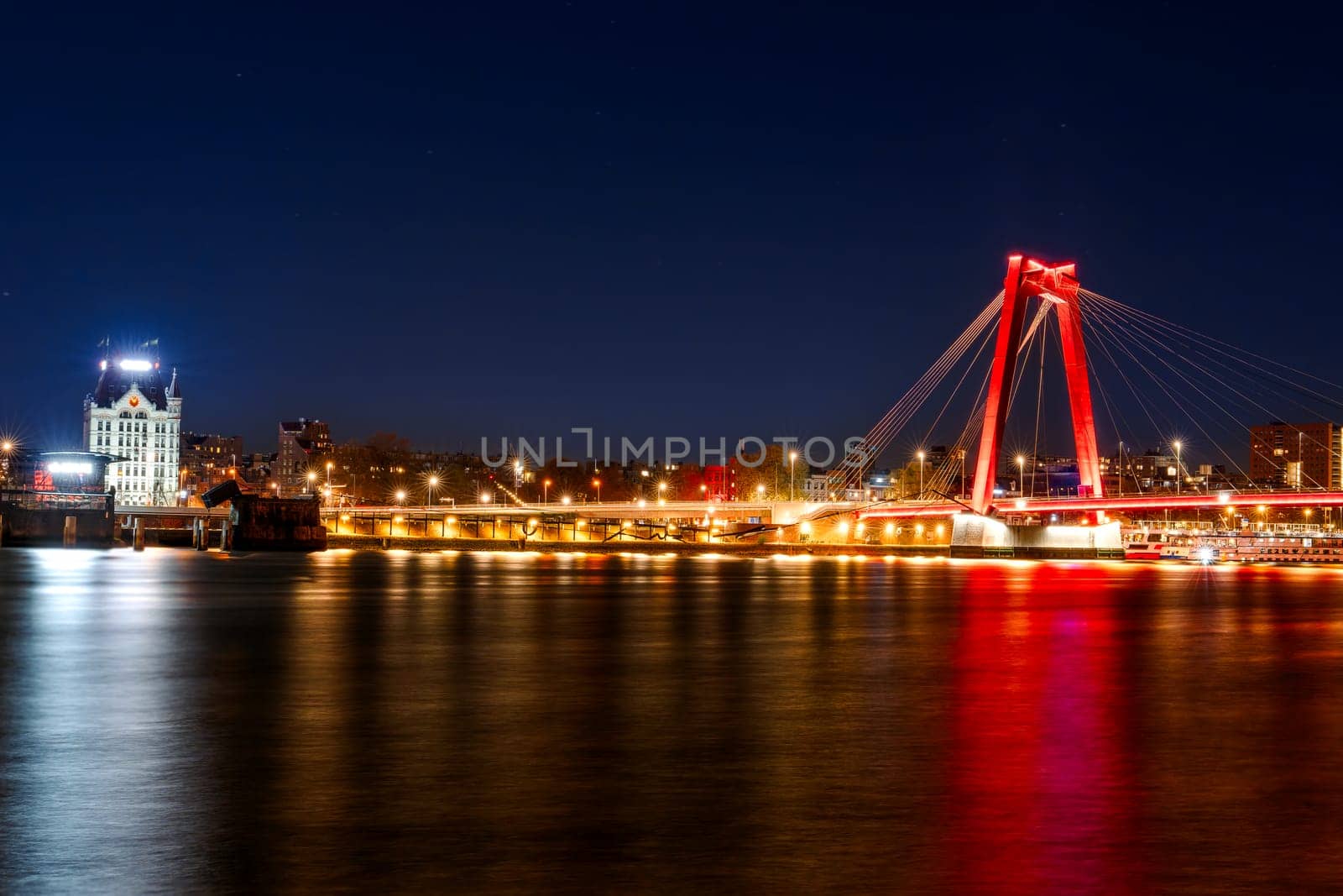Capture the breathtaking beauty of Willemsbrug bridge in Rotterdam with this stunning long exposure night photo. The colorful lights reflecting on the water add a magical touch to the urban landscape.