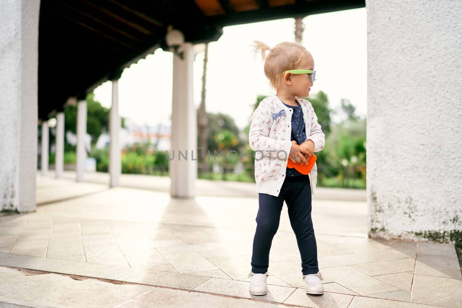 Little girl in sunglasses stands half-turned in a gazebo in the garden. High quality photo