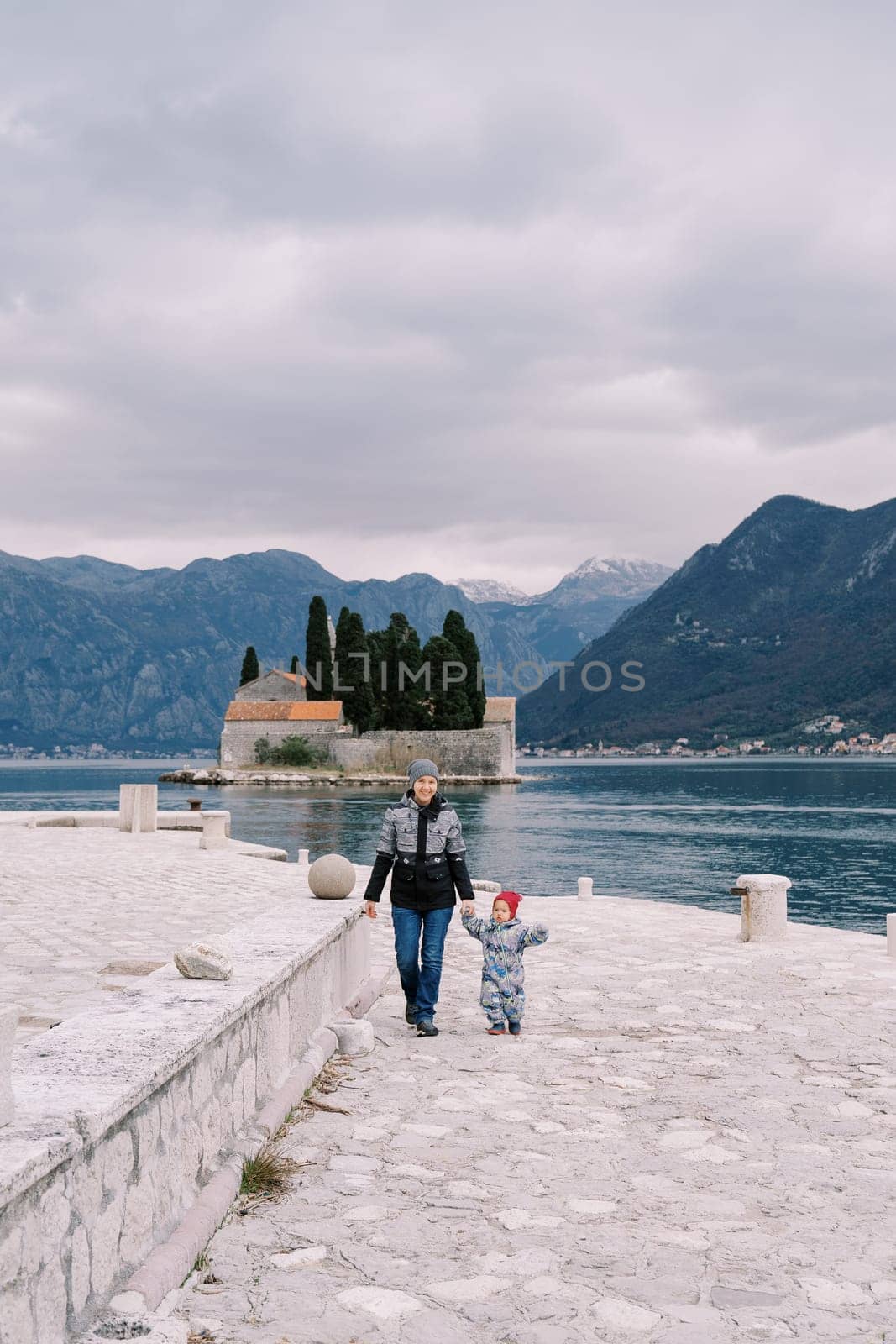 Mother with a small child walk holding hands along the pier with St. George Island in the background. Montenegro. High quality photo