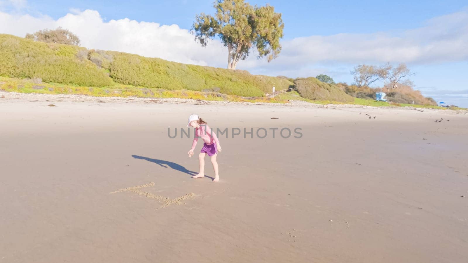 A little girl joyfully plays on the vast, empty sands of El Capitan State Beach in California during winter.