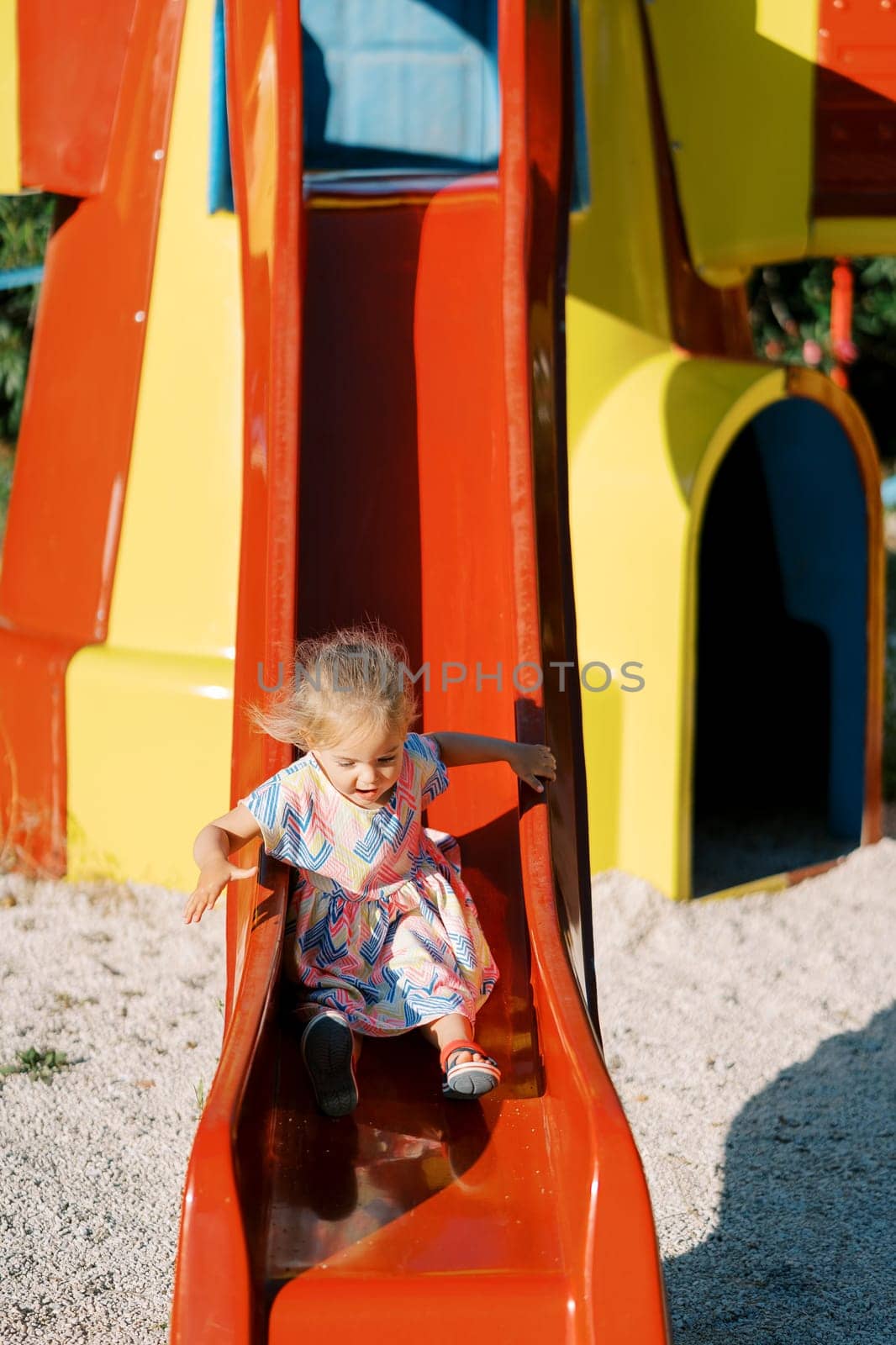 Little girl with flying hair slides down a slide holding onto a handrail. High quality photo