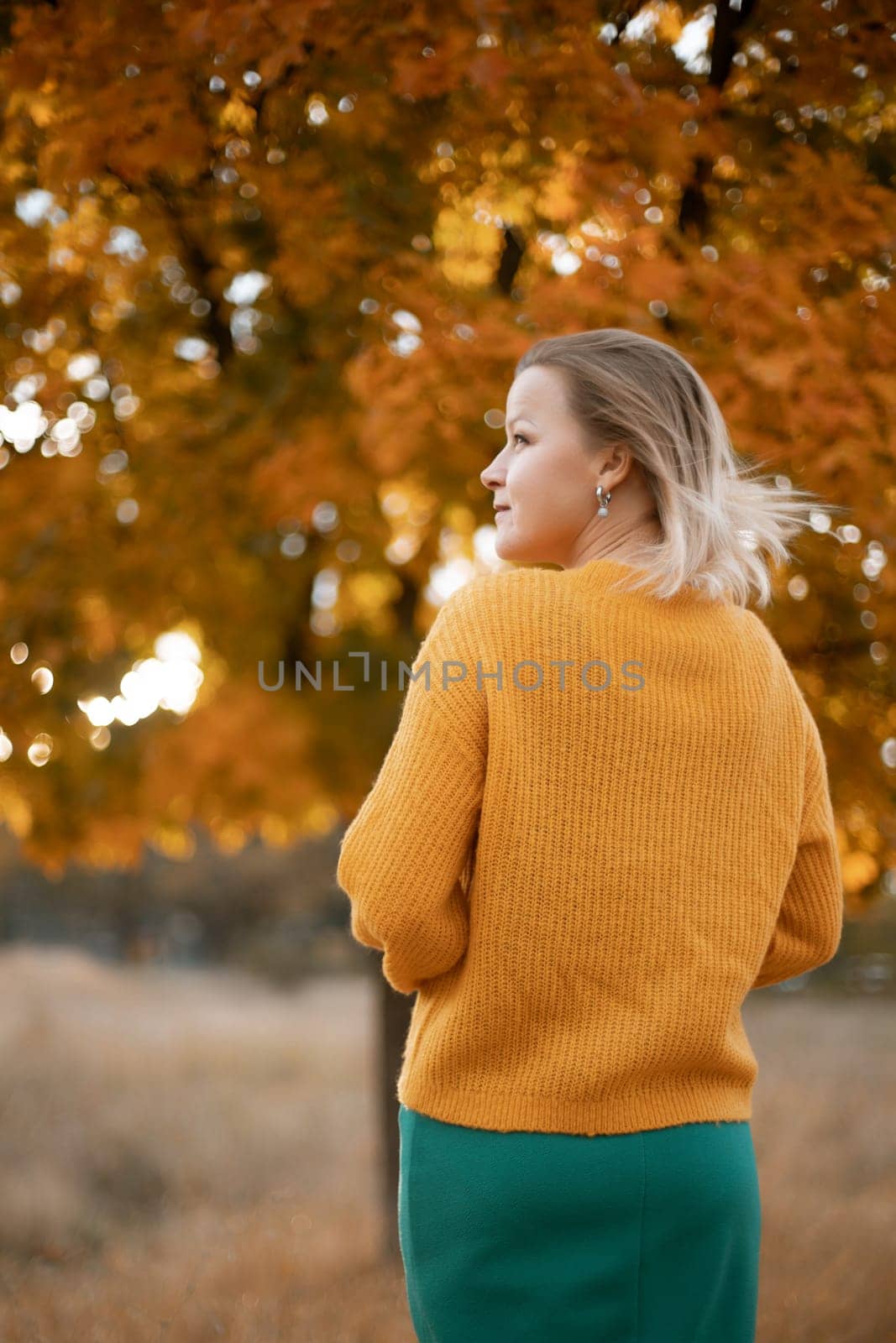 autumn woman in a yellow sweater and green skirt, against the background of an autumn tree.