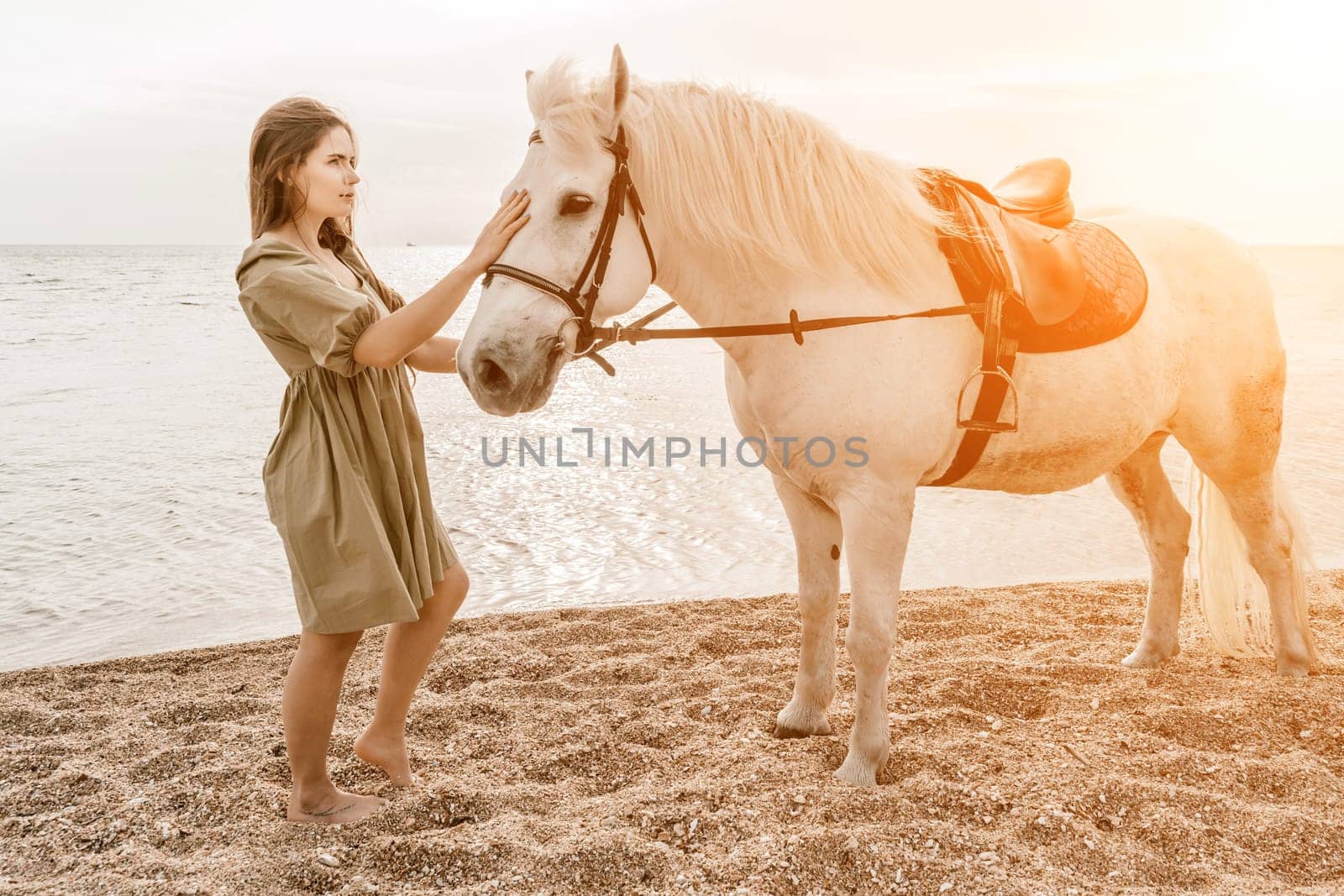 A woman in a dress stands next to a white horse on a beach, with the blue sky and sea in the background