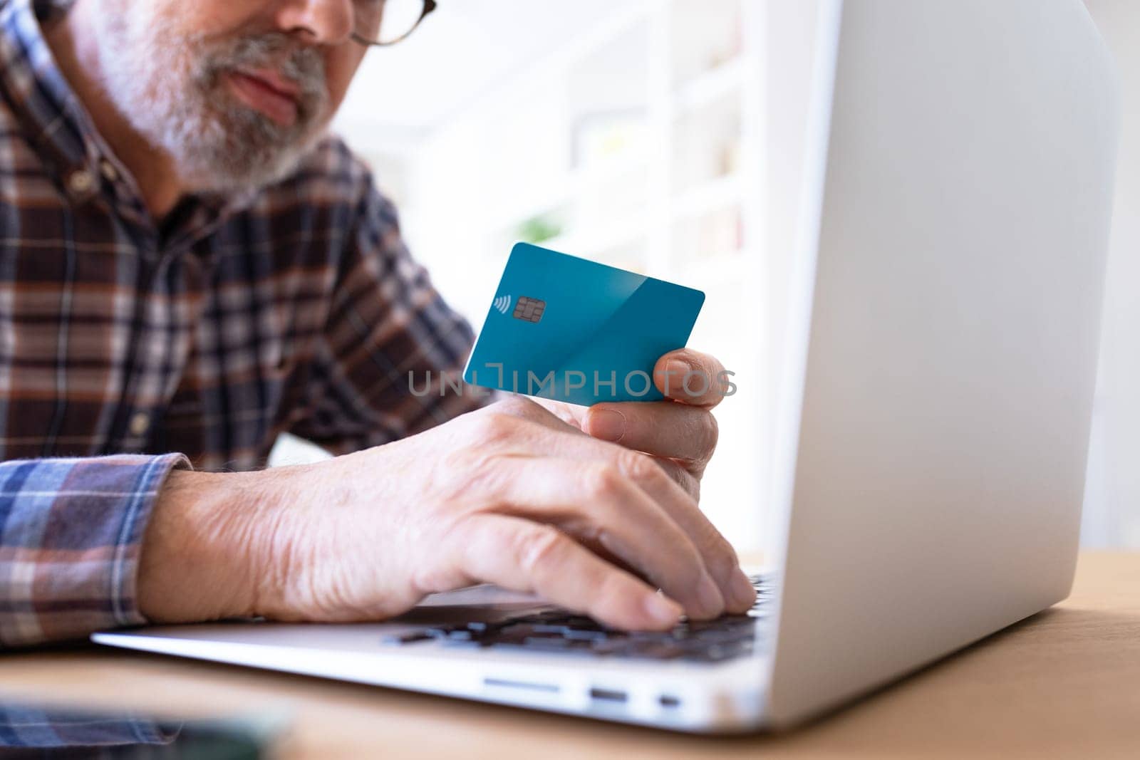Close up of senior man hands holding credit card while shopping online using laptop. by Hoverstock