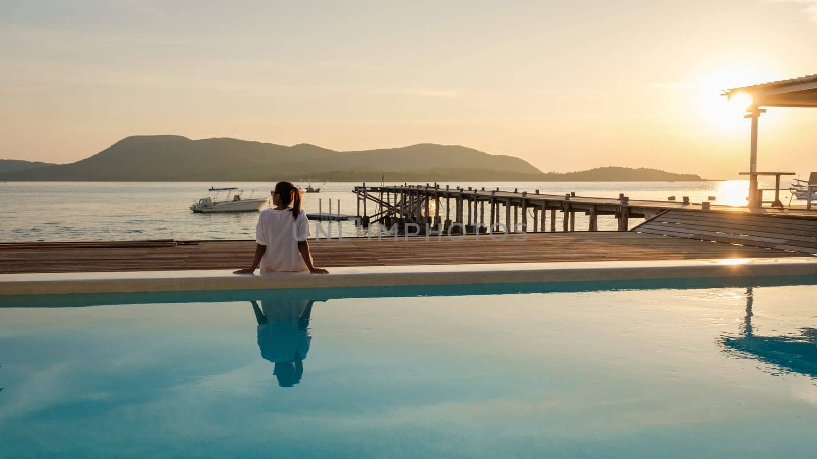 Asian woman watching the sunset at a wooden pier by the swimming pool in the ocean during sunset in Samaesan Thailand