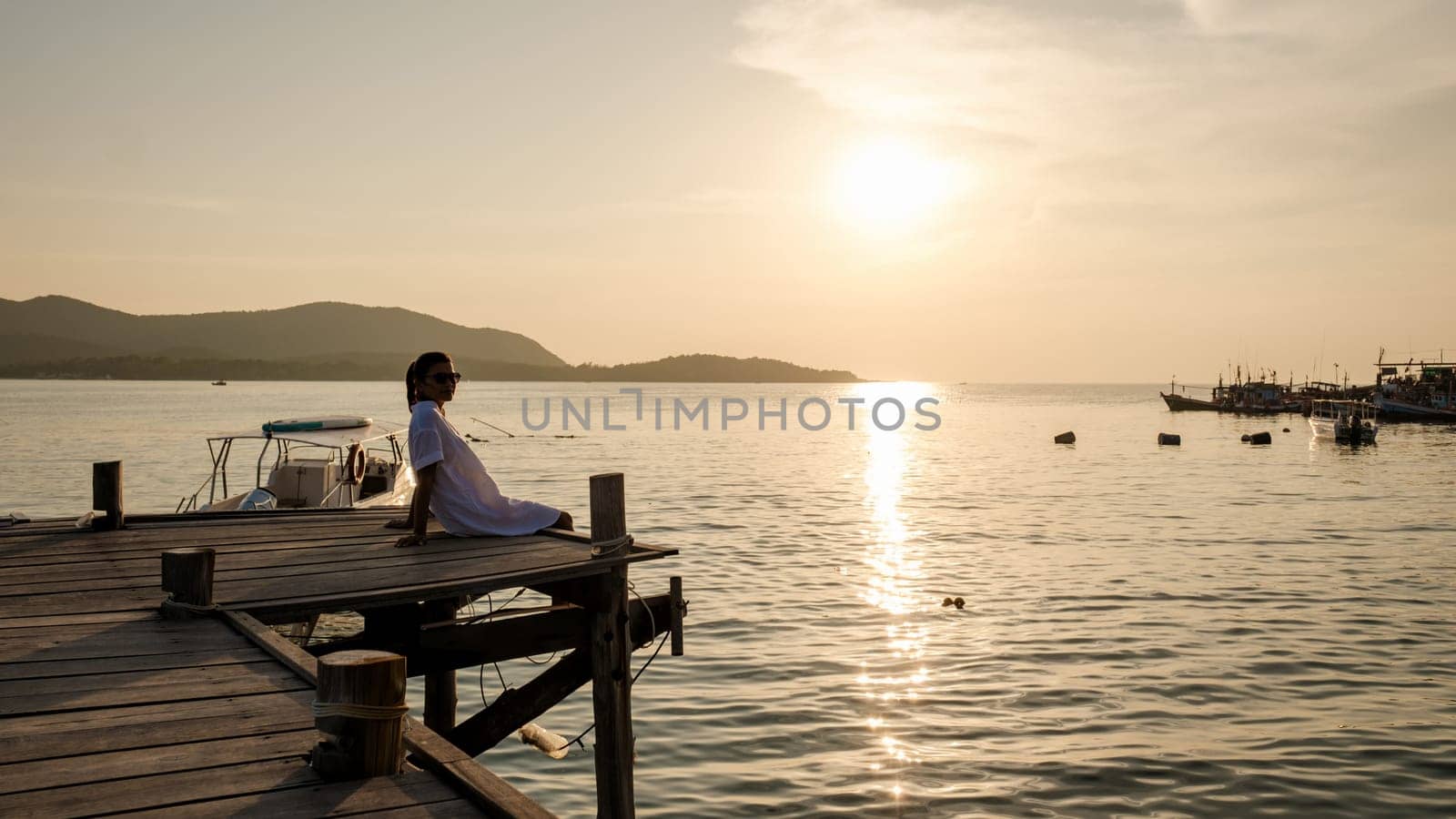 Asian woman watching sunset at a wooden pier in the ocean during sunset in Samaesan Thailand by fokkebok