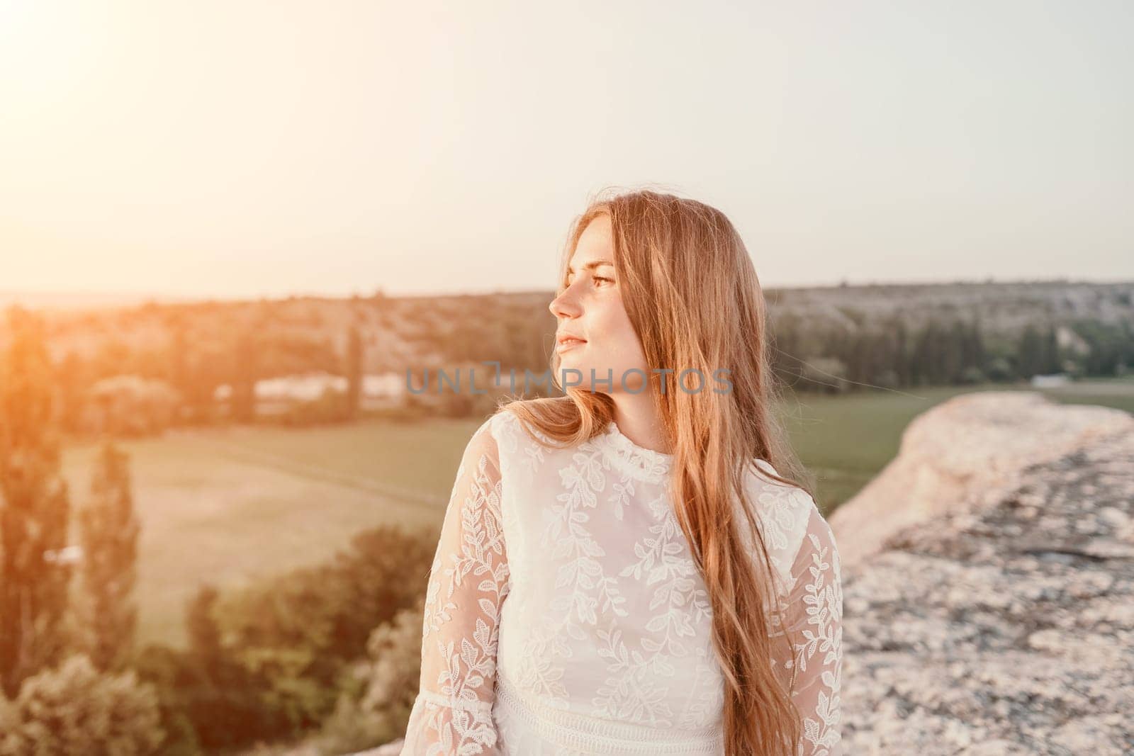 Happy woman in white boho dress on sunset in mountains. Romantic woman with long hair standing with her back on the sunset in nature in summer with open hands. Silhouette. Nature. Sunset. by panophotograph