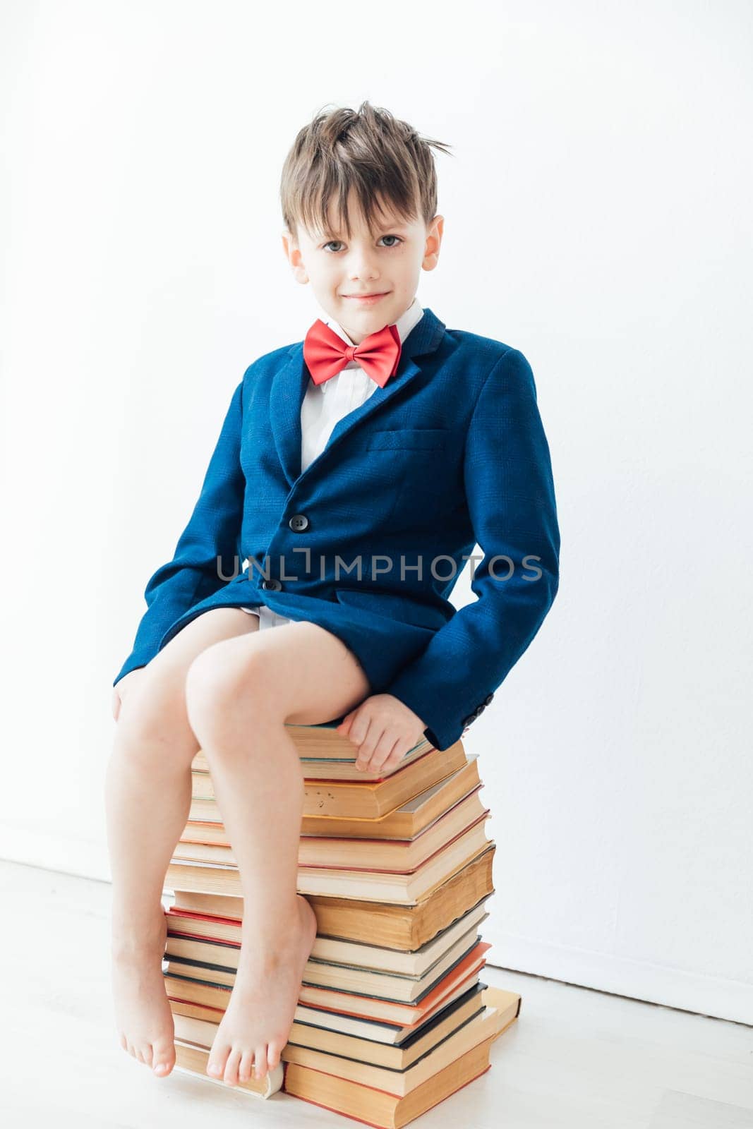 Boy in jacket and bow tie sitting on a stack of books