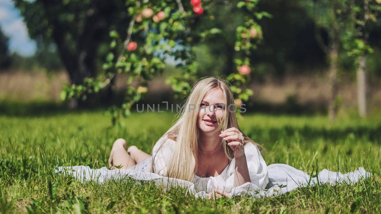 A blonde girl lies in a clearing in an apple orchard