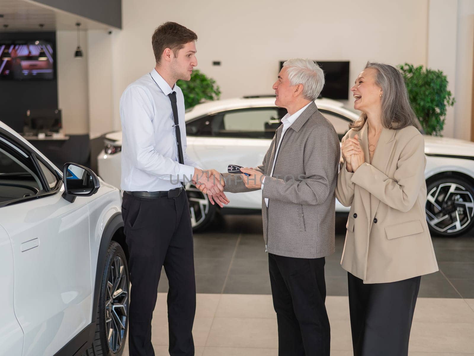 A salesman hands over the keys to a new car to an elderly Caucasian couple. by mrwed54